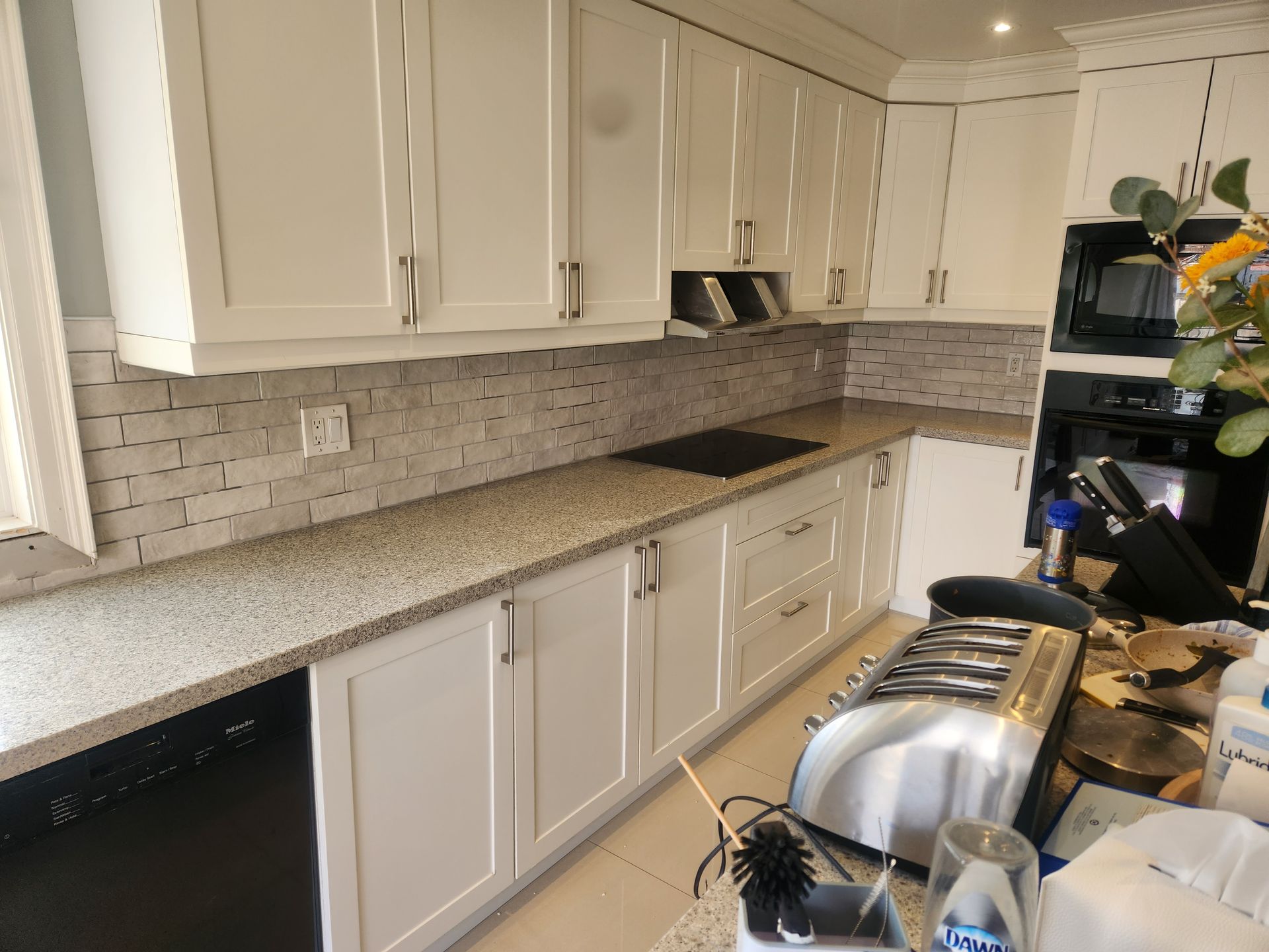 White kitchen with light countertops, brick backsplash, and cabinets.