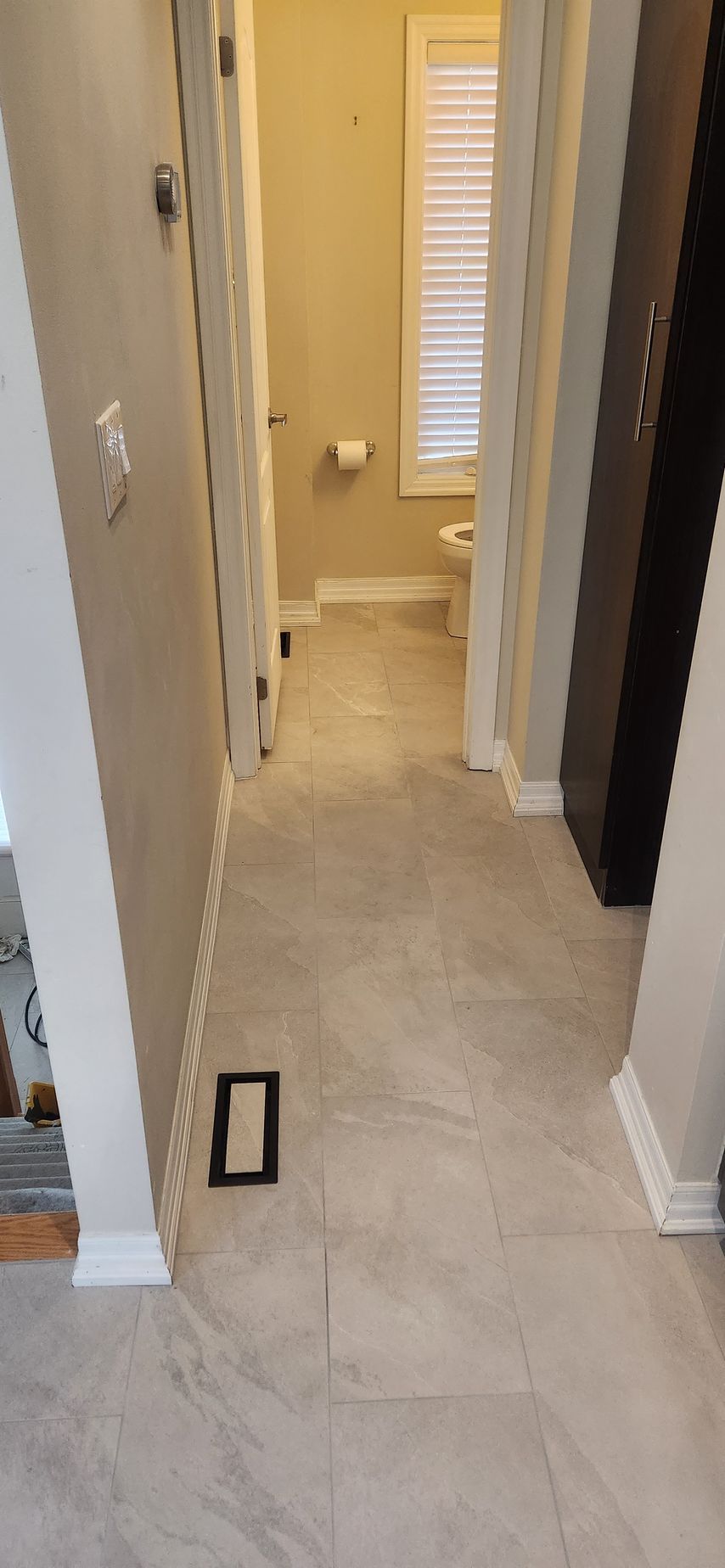 Hallway with light tile floor, open bathroom door, and dark cabinet.