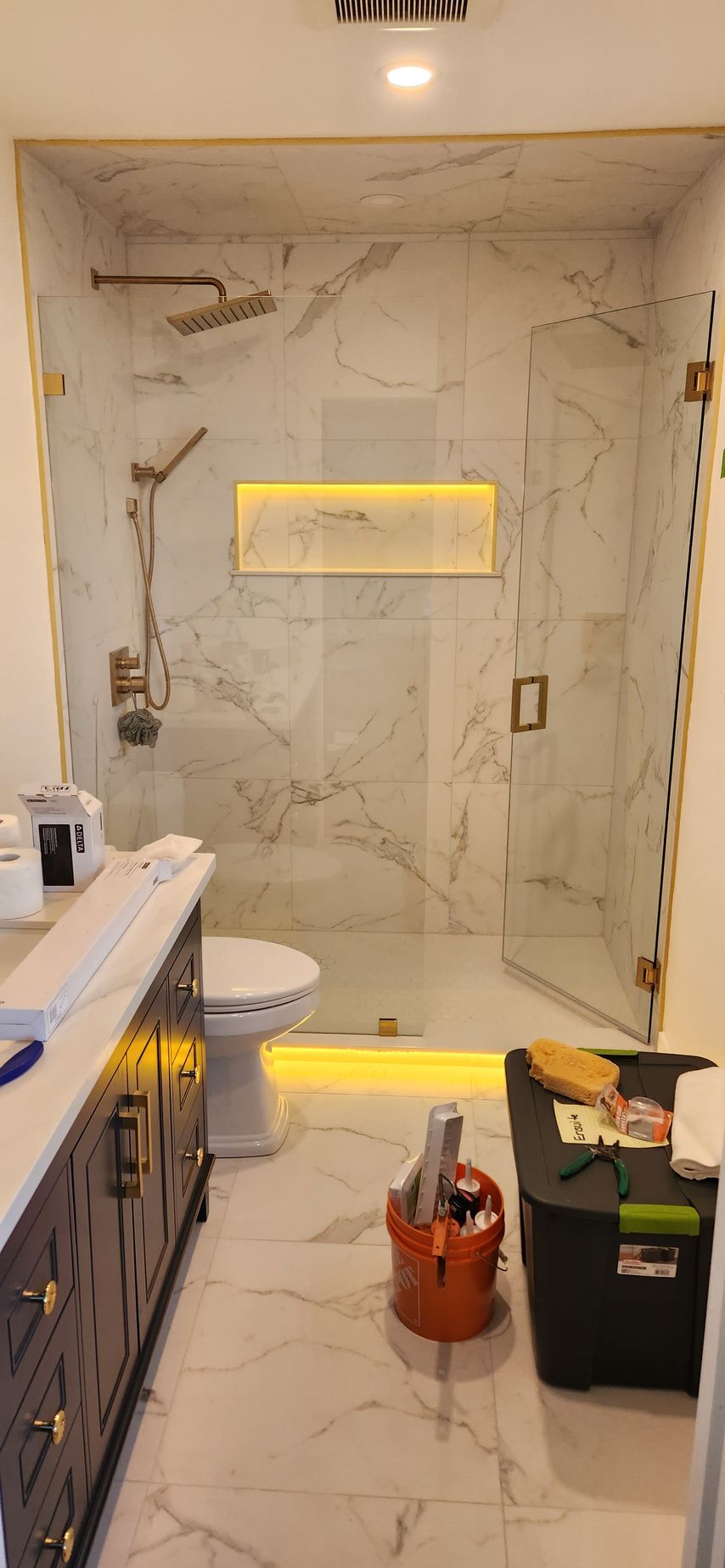 Modern bathroom with marble walls, a glass shower door, and gold fixtures.
