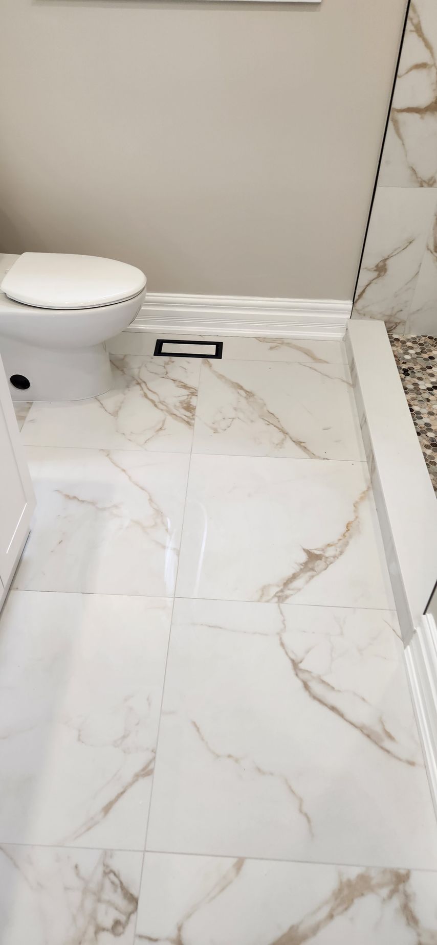 Bathroom with white and gold marble tile flooring, white toilet, and walls.