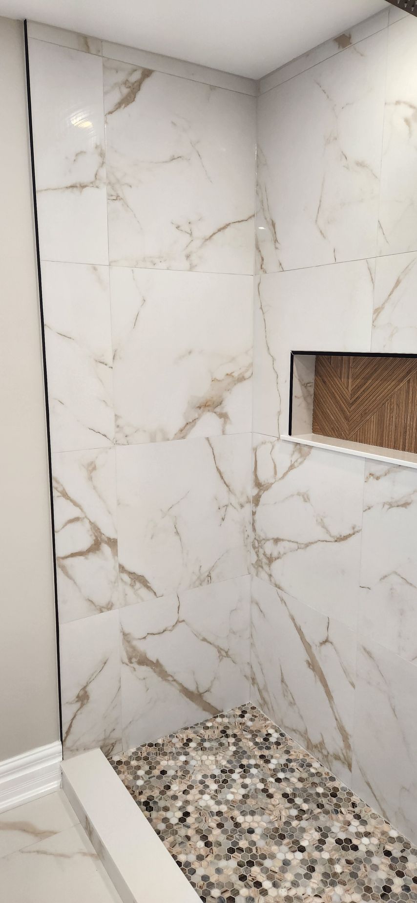 White marble shower with pebble floor, accent niche.