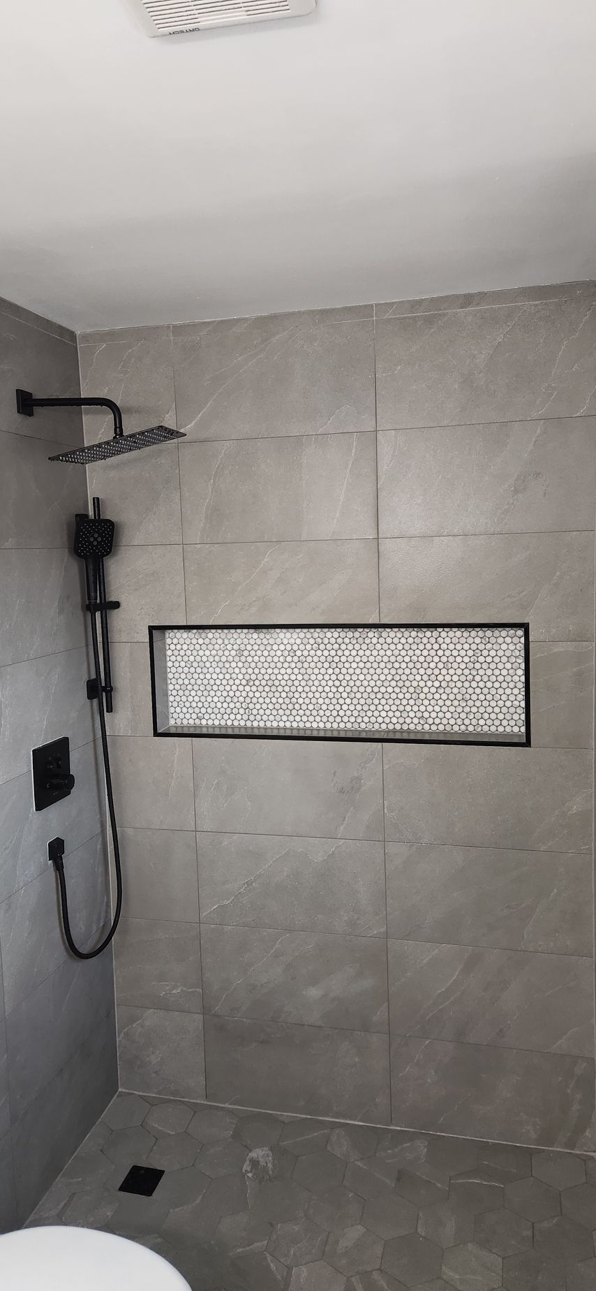 Bathroom with gray tiles, black shower fixtures, and a recessed shelf.