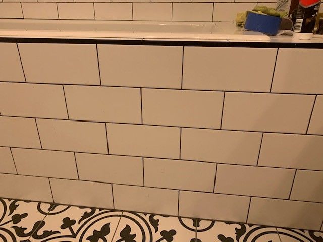 White rectangular tiles on a bathtub surround with black grout, patterned floor.
