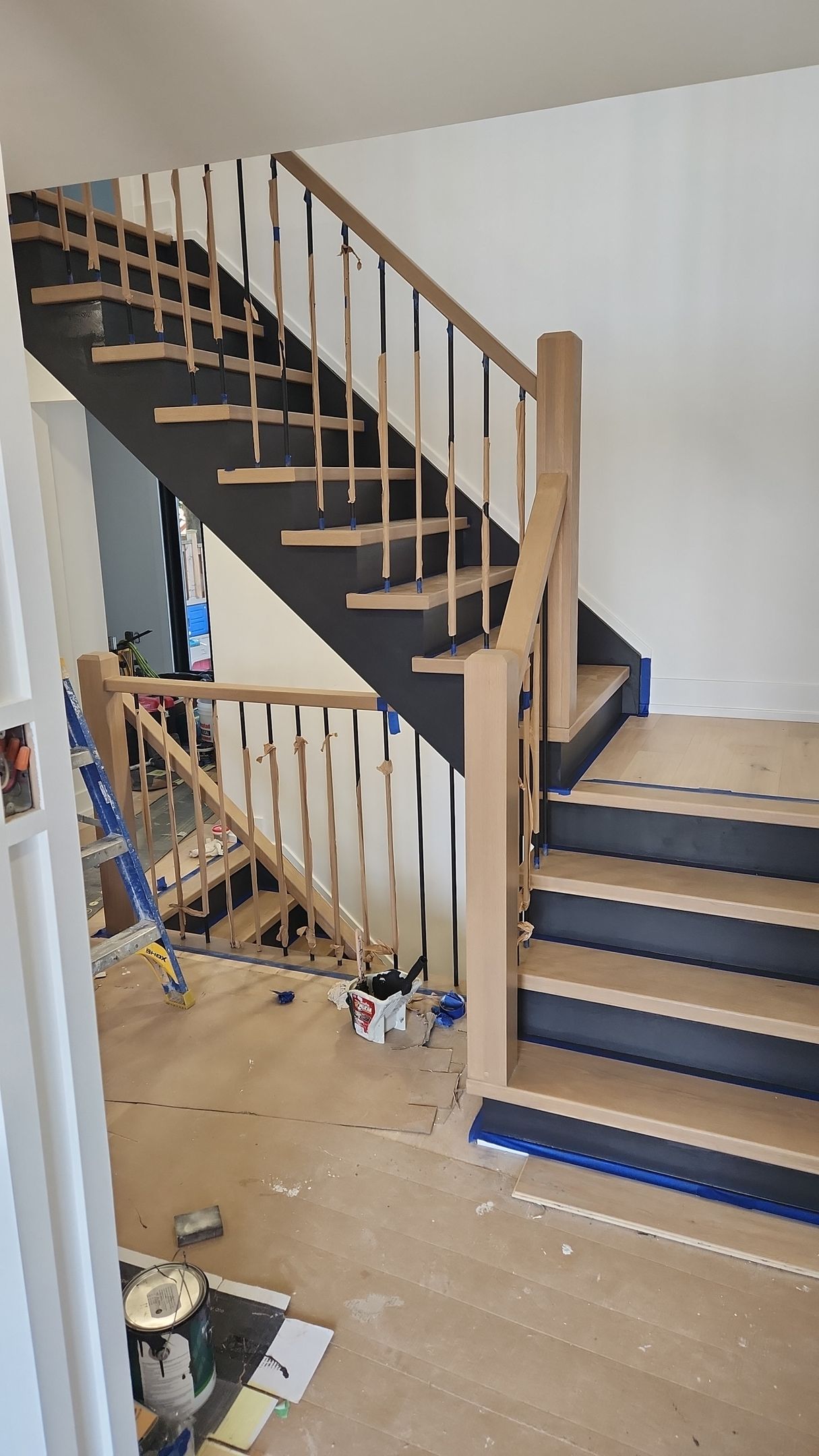 Wooden staircase under construction, featuring dark steps, light wood railings, and white walls.