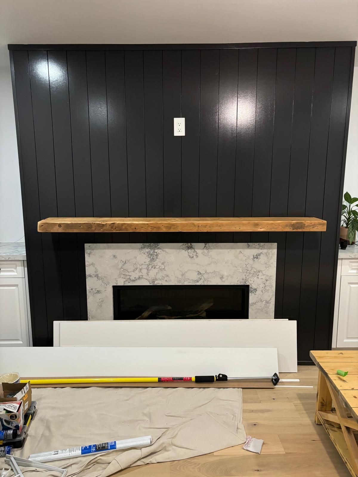 Black paneled wall with floating wood mantle, concrete fireplace, and white trim pieces.