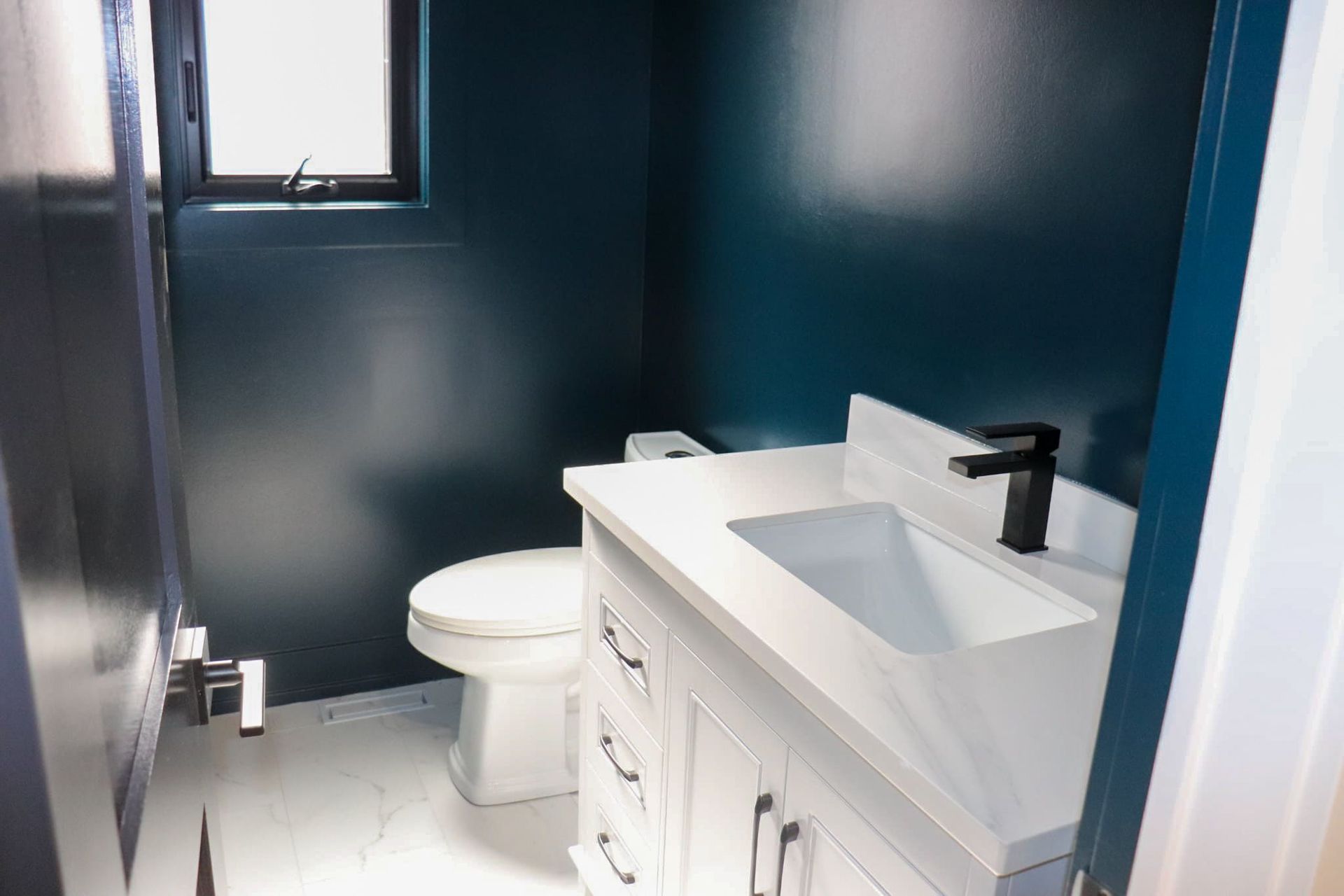 A small, modern bathroom with a white vanity, toilet, and dark blue walls.