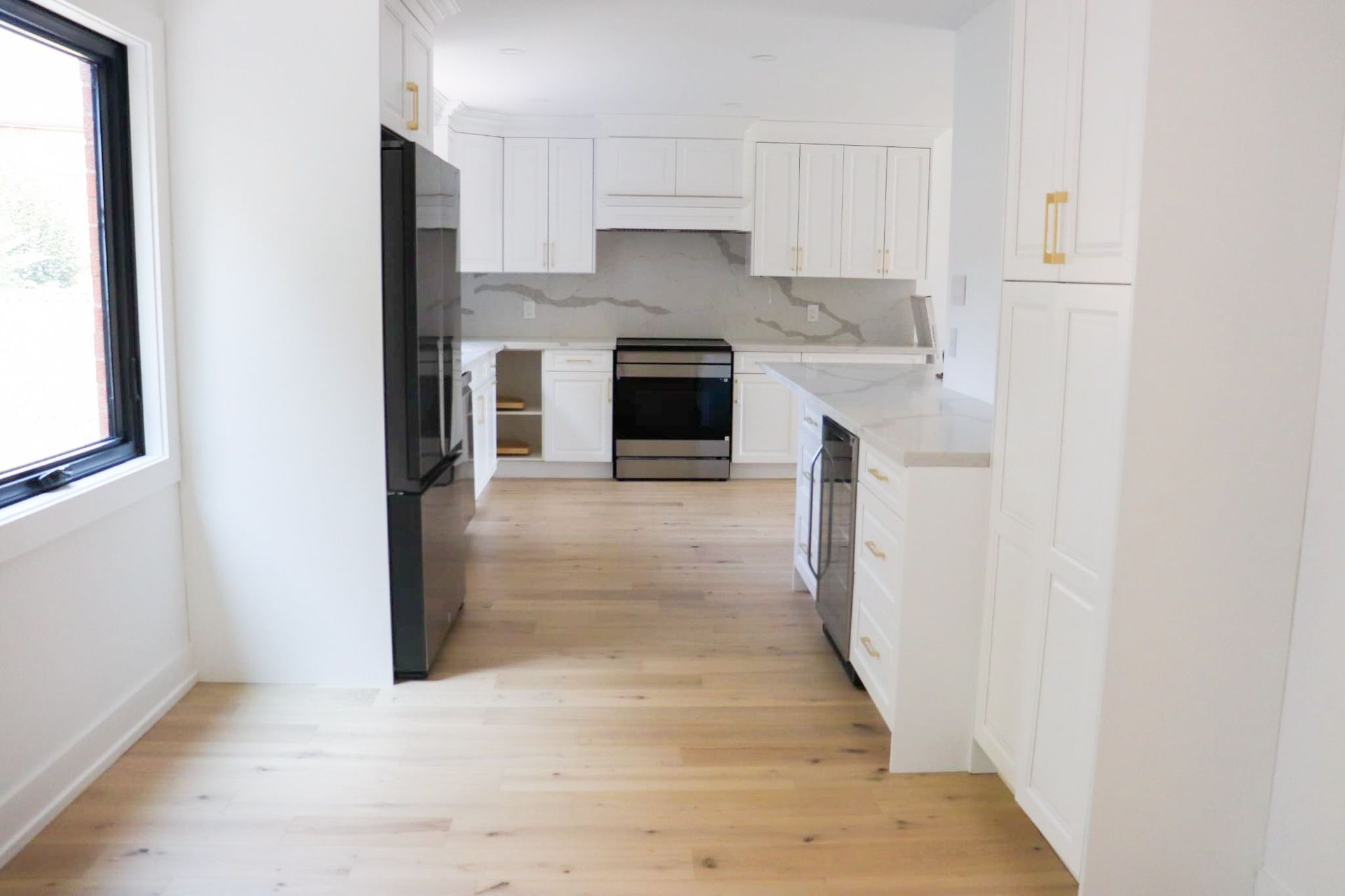 Bright white kitchen with wood floors, black refrigerator, and marble backsplash.