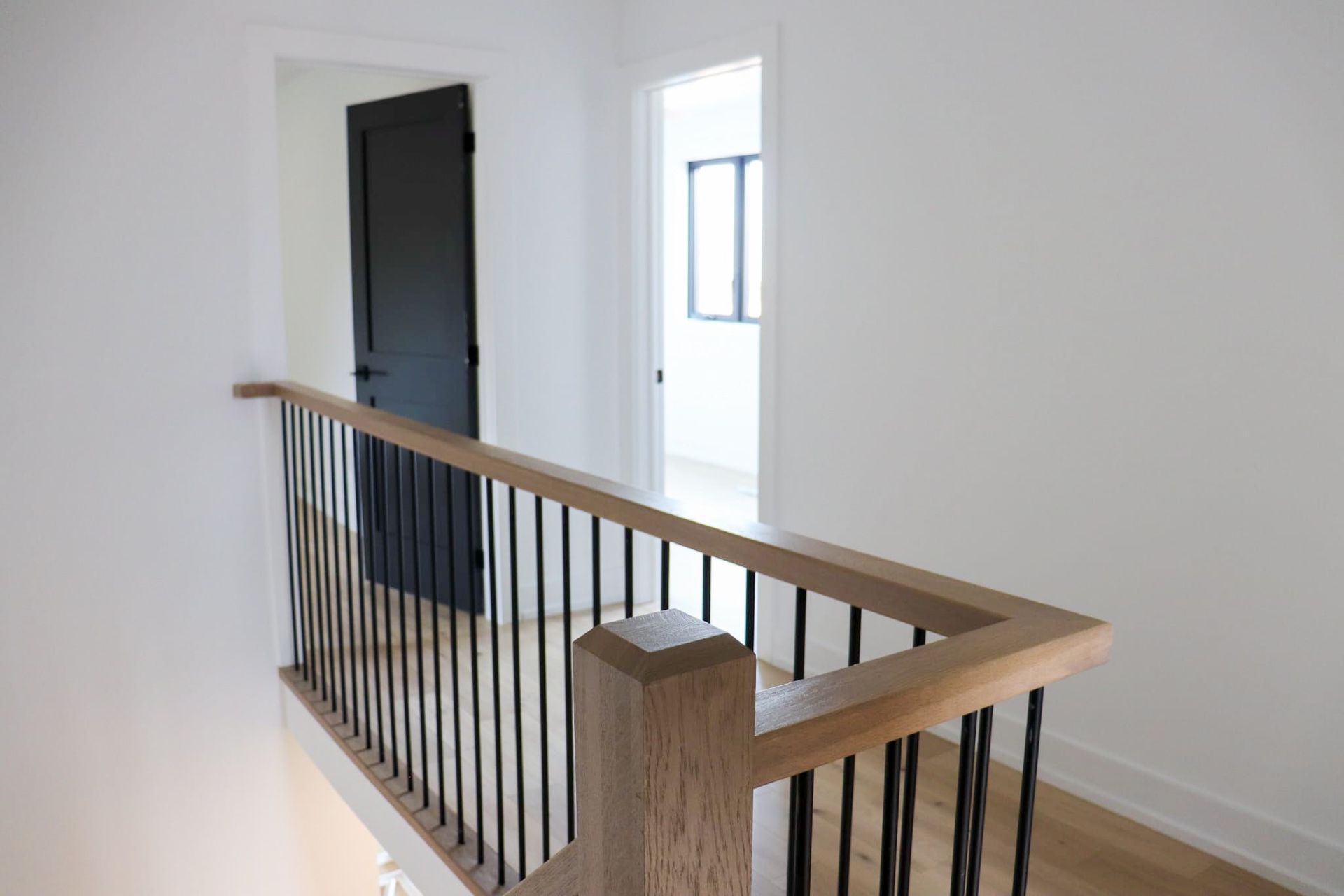 Hallway with wooden railing and black iron bars, leading to a black door and a room with a window.