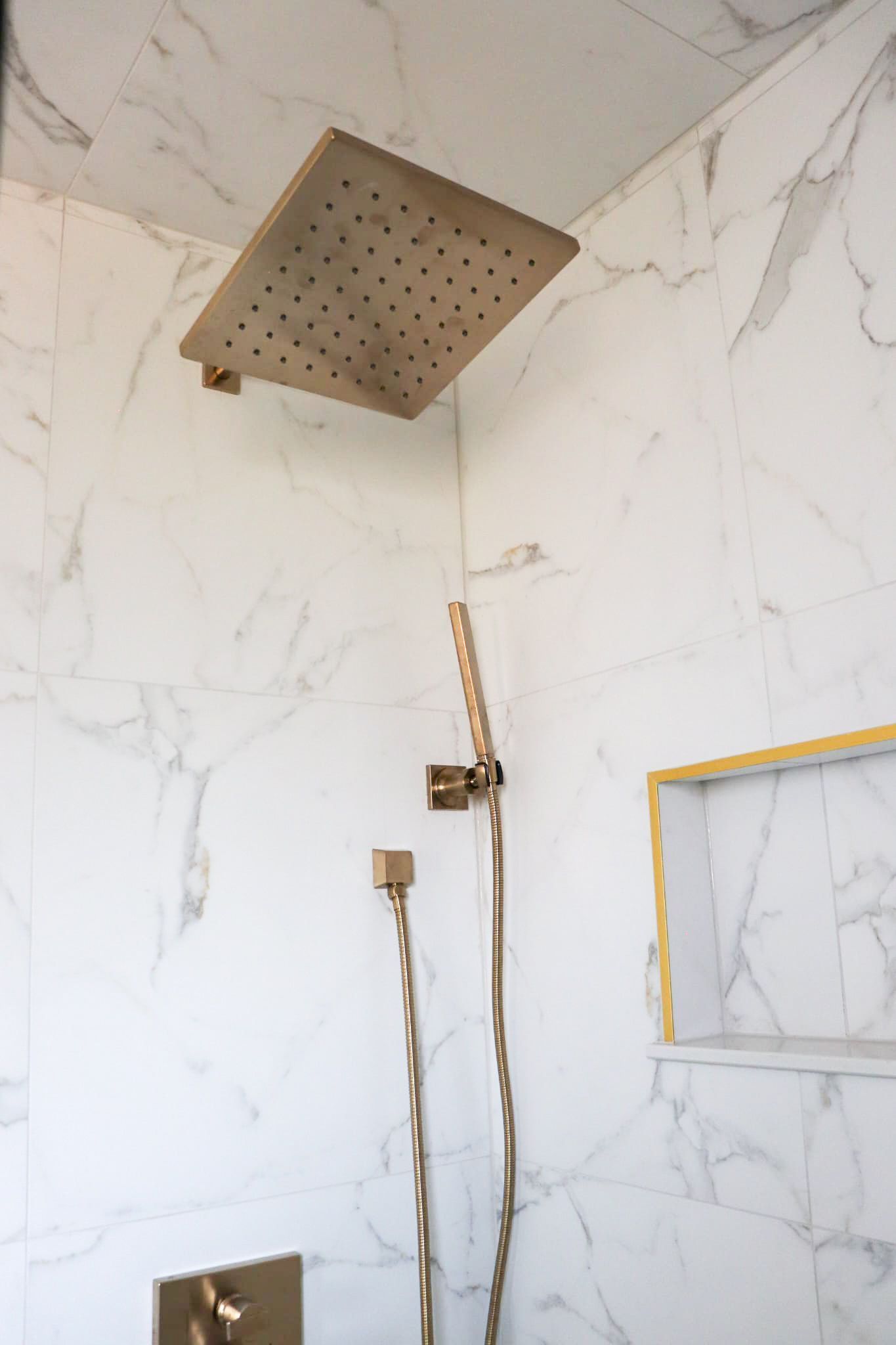 Gold shower fixtures against white marble tile in a shower.