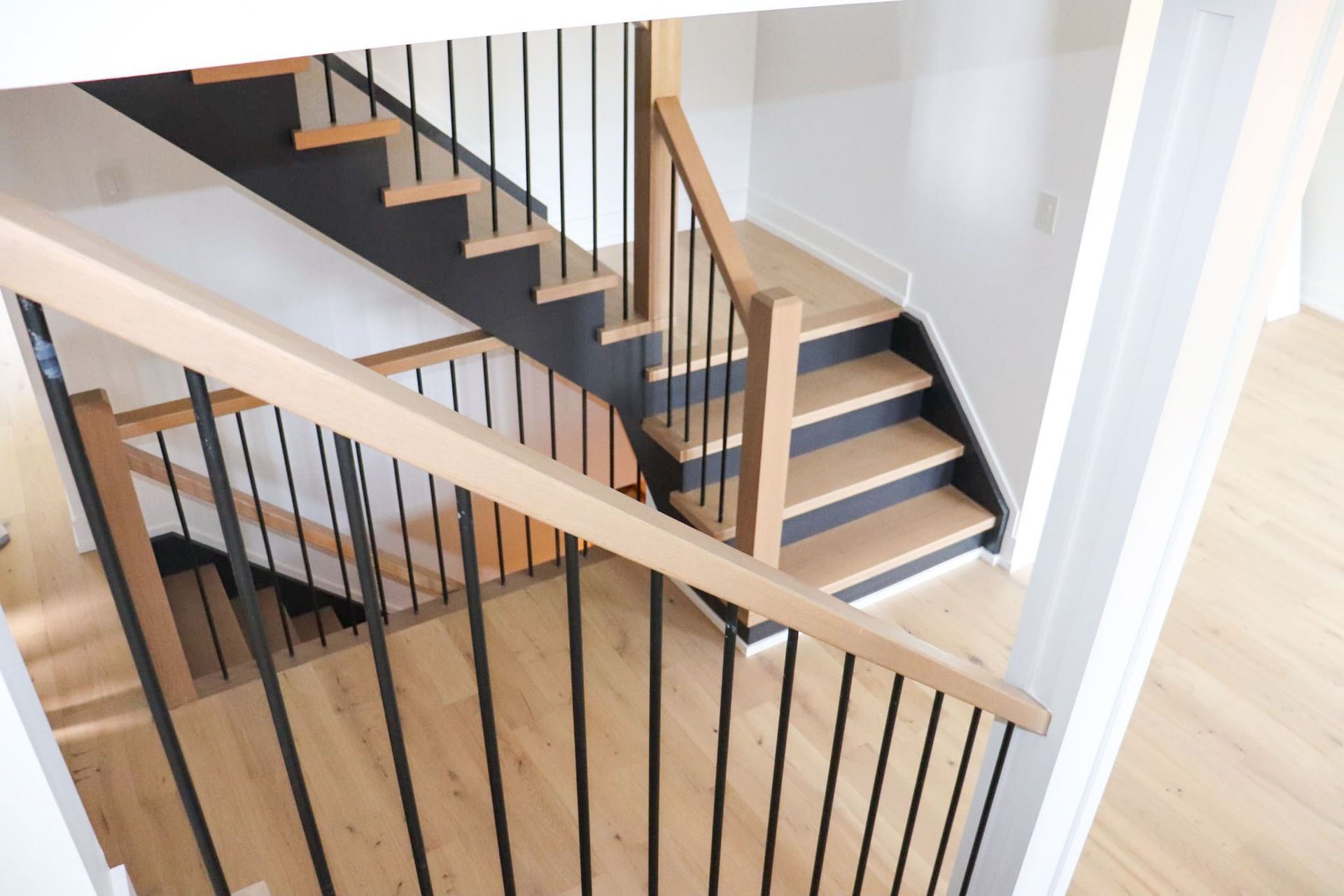 Wooden staircase with black metal railings and light wood floors.