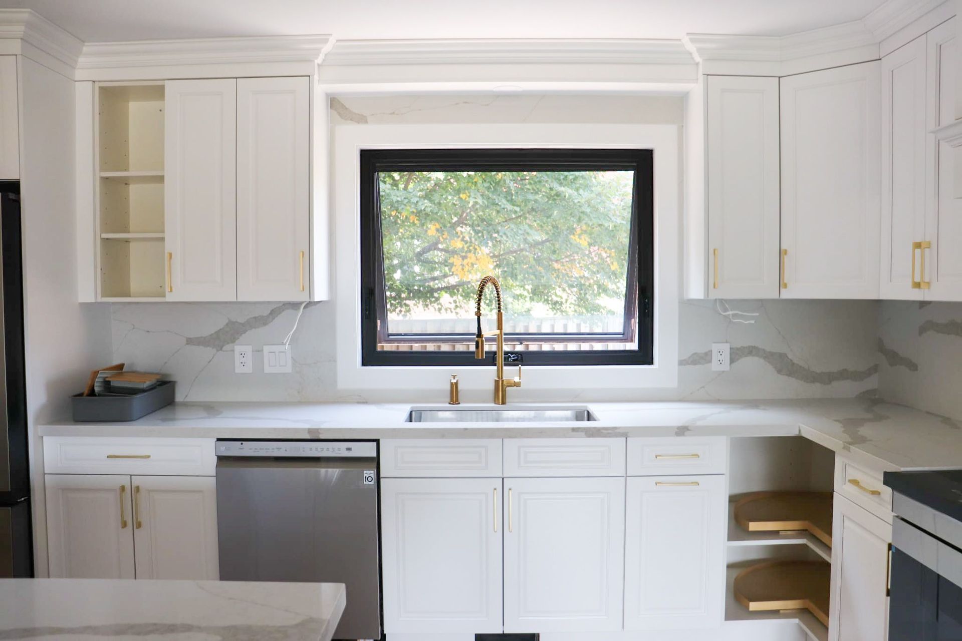 White kitchen with marble countertops, gold faucet, and black window frame.