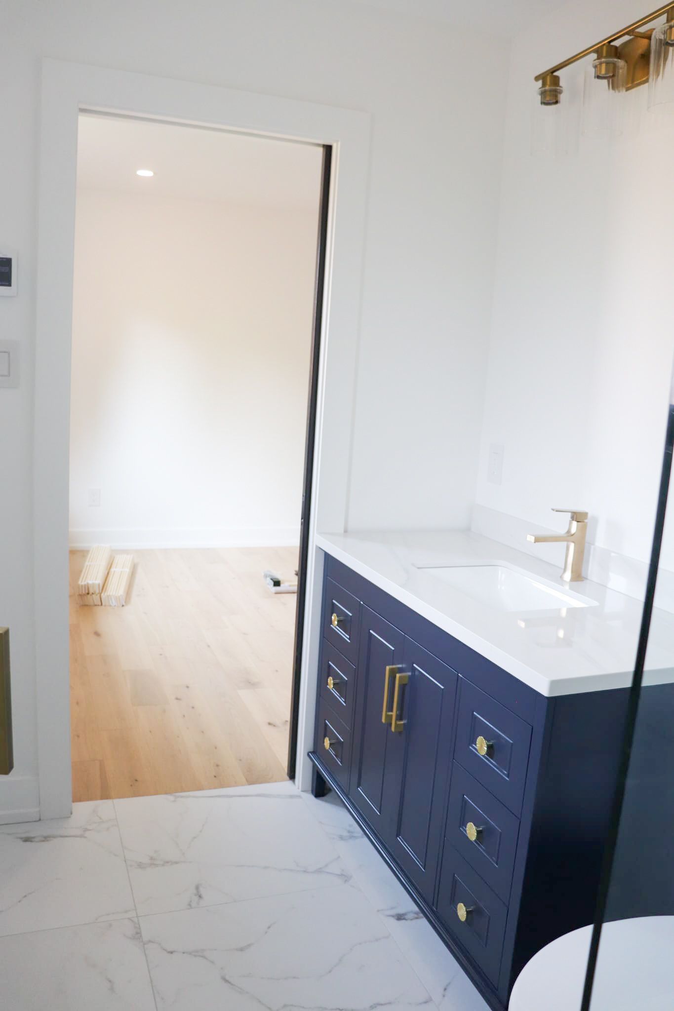 Navy blue vanity in bathroom with marble flooring. Open door to hardwood floors.
