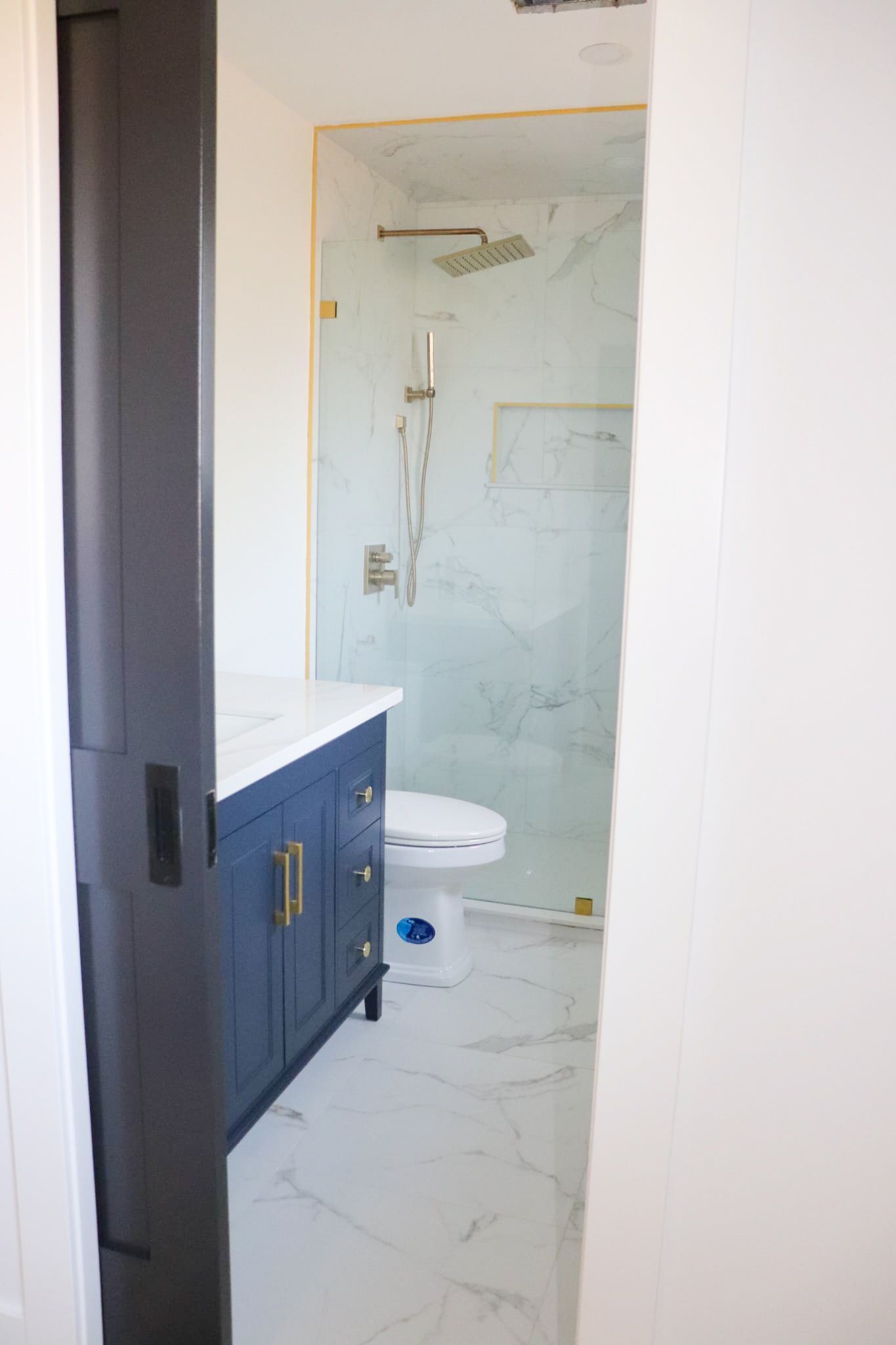Bathroom with blue vanity, marble floor, and glass shower door.