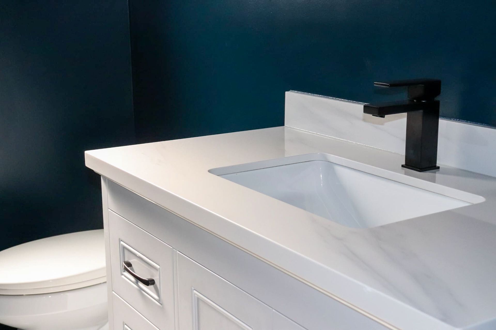 White bathroom vanity with a sink and black faucet, teal wall in the background.