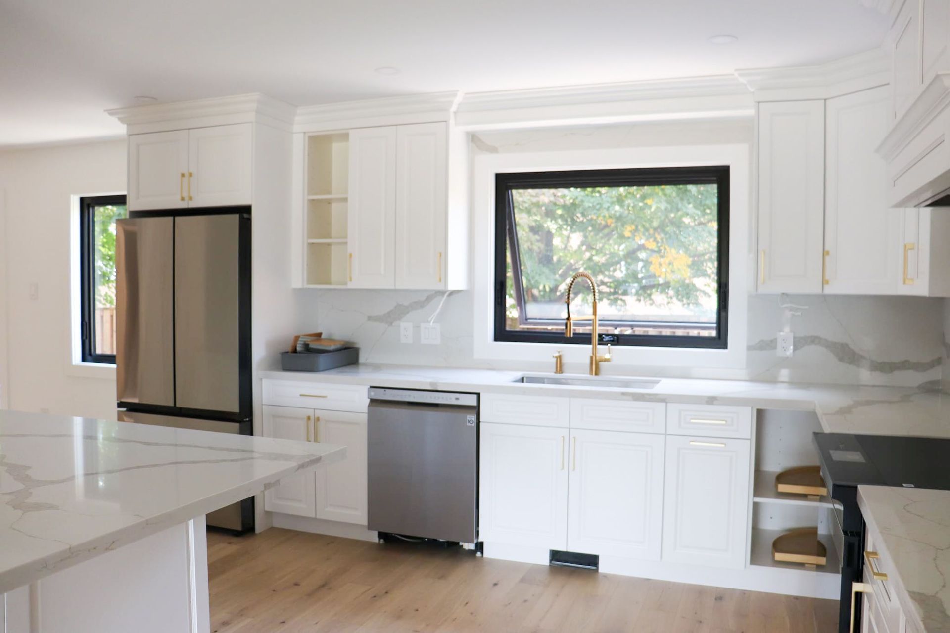 White kitchen with stainless steel appliances, gold fixtures, and marble countertops.