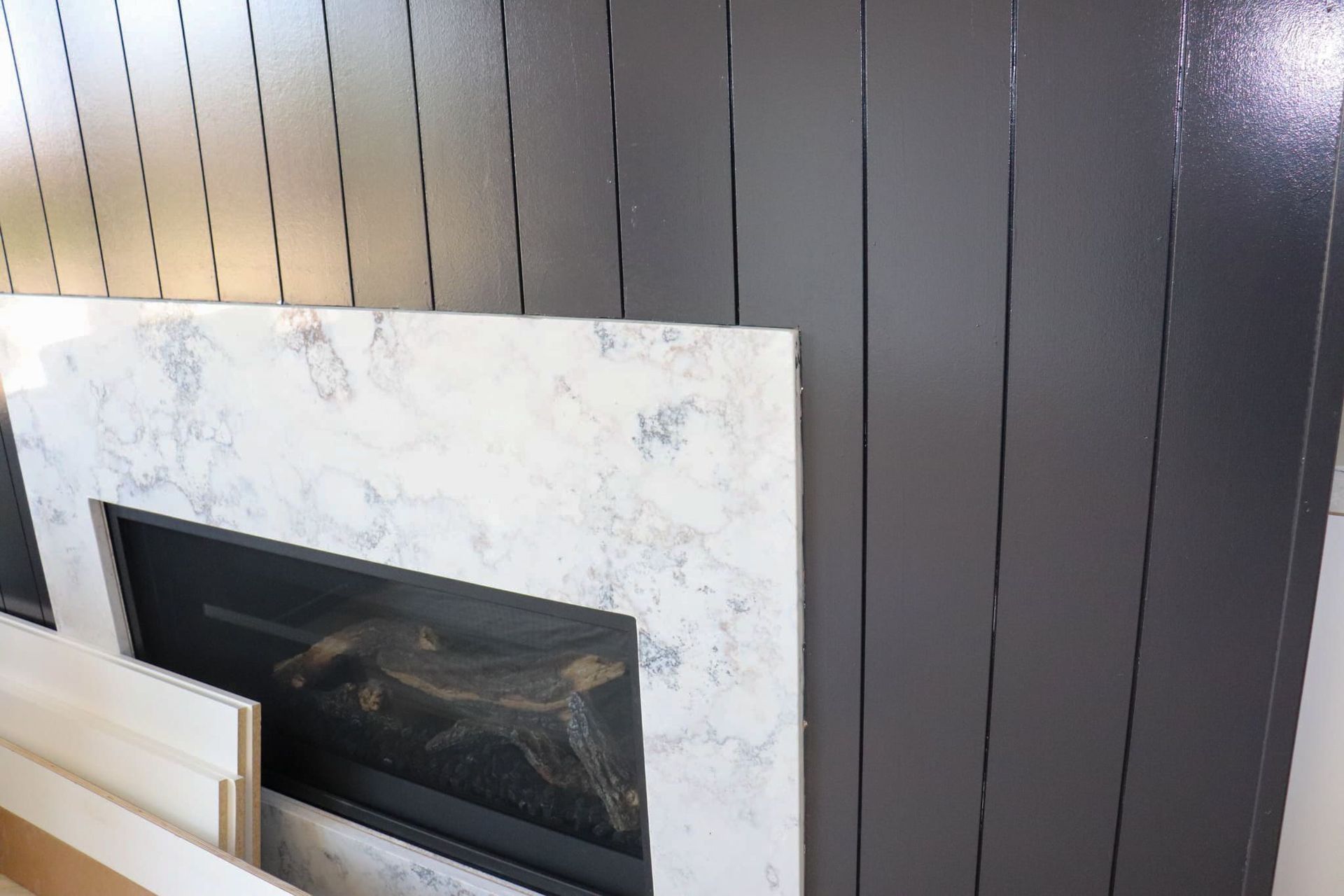 Fireplace with marble surround next to dark grey vertical paneling.
