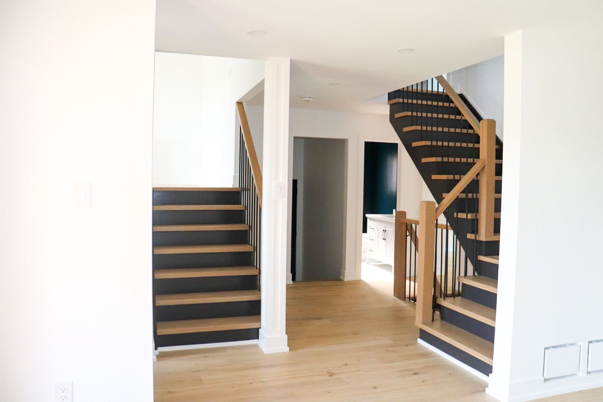 Two staircases, one straight, one turning, with black and wood steps, leading to different levels of a home.