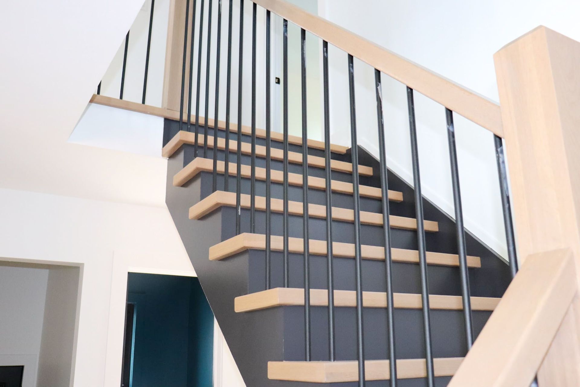 Staircase with wooden steps, black sides, and black metal railings.