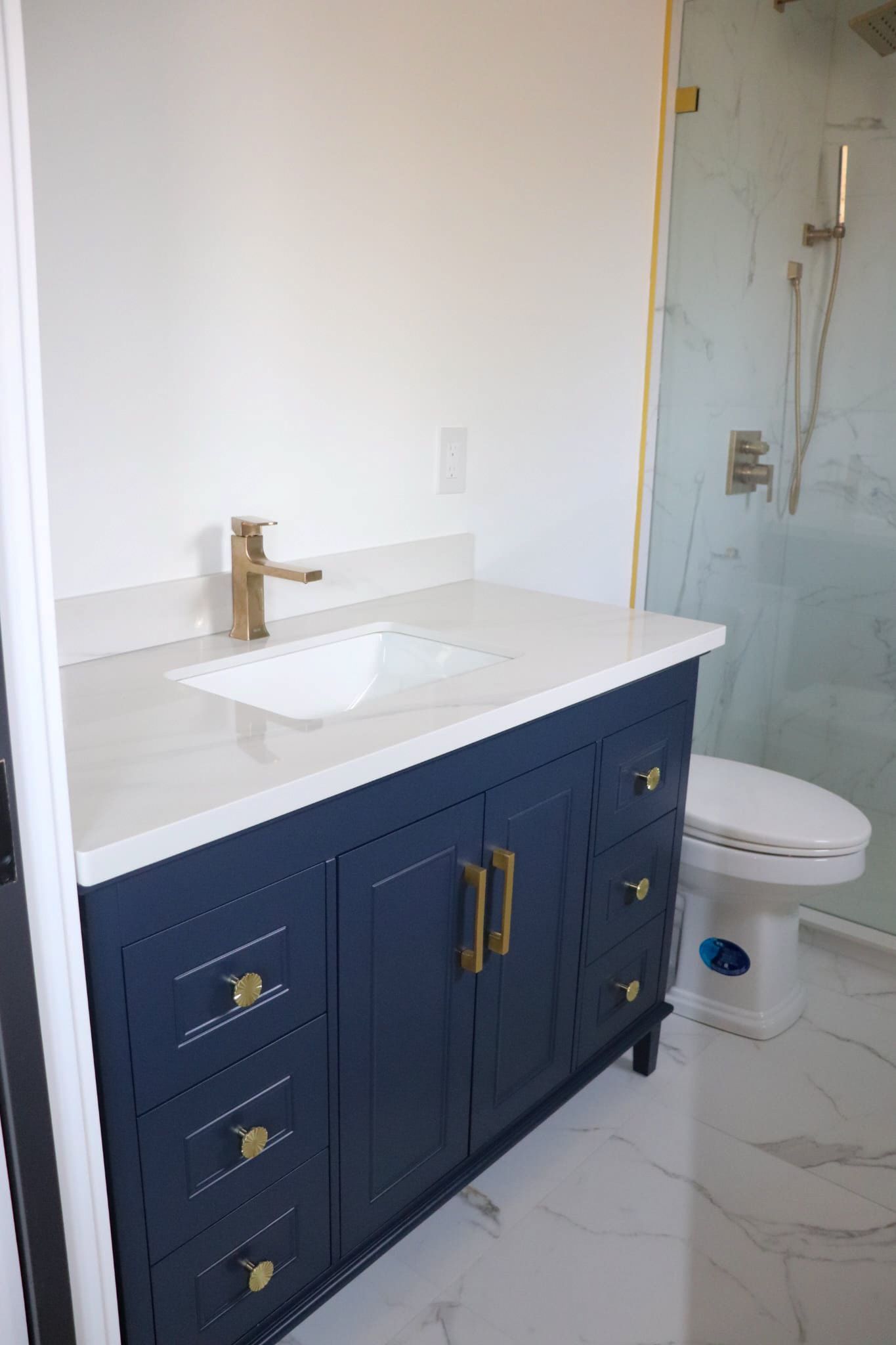 Navy blue bathroom vanity with gold hardware and a white countertop. Toilet and shower visible.