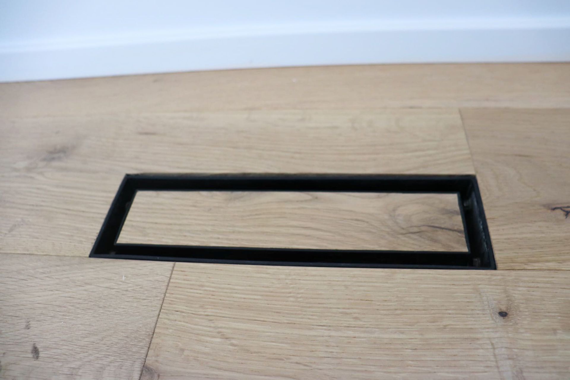 Black rectangular floor vent on light wood flooring.