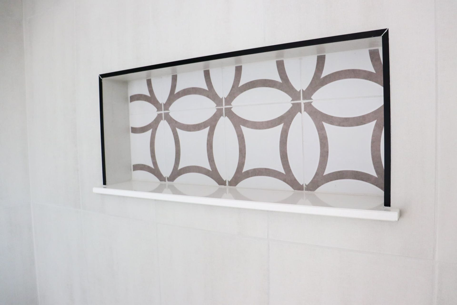 Recessed shelf in white wall with patterned tile backing. Black frame, white shelf.
