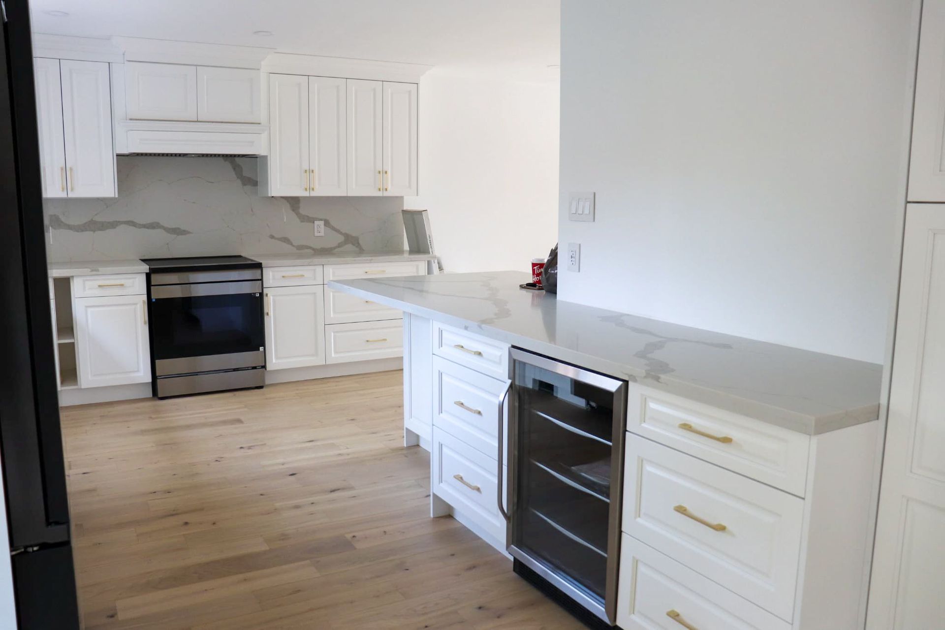White kitchen with marble countertops, stainless steel appliances, and light wood floors.