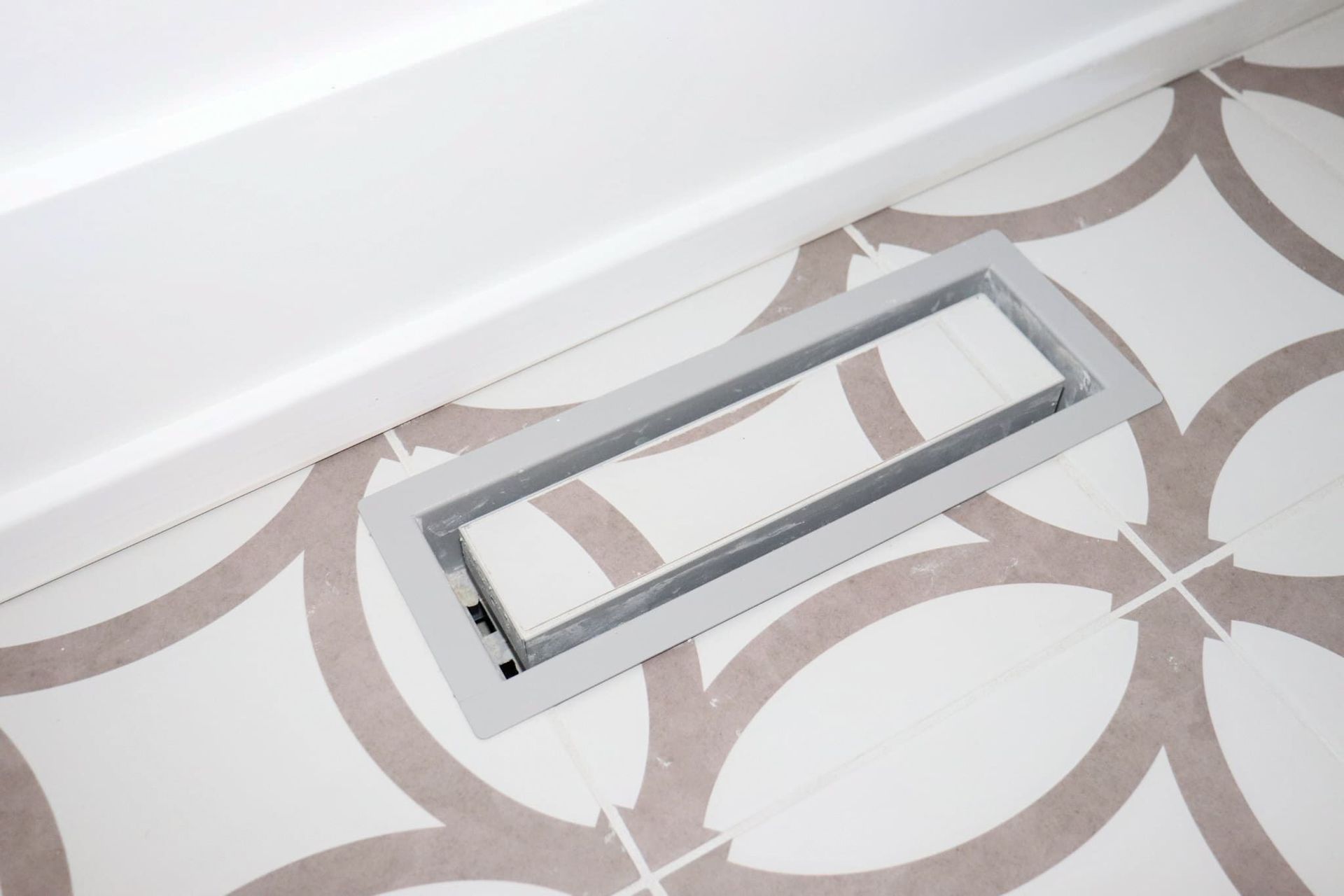 Floor vent against a white wall, set in a patterned tile floor.