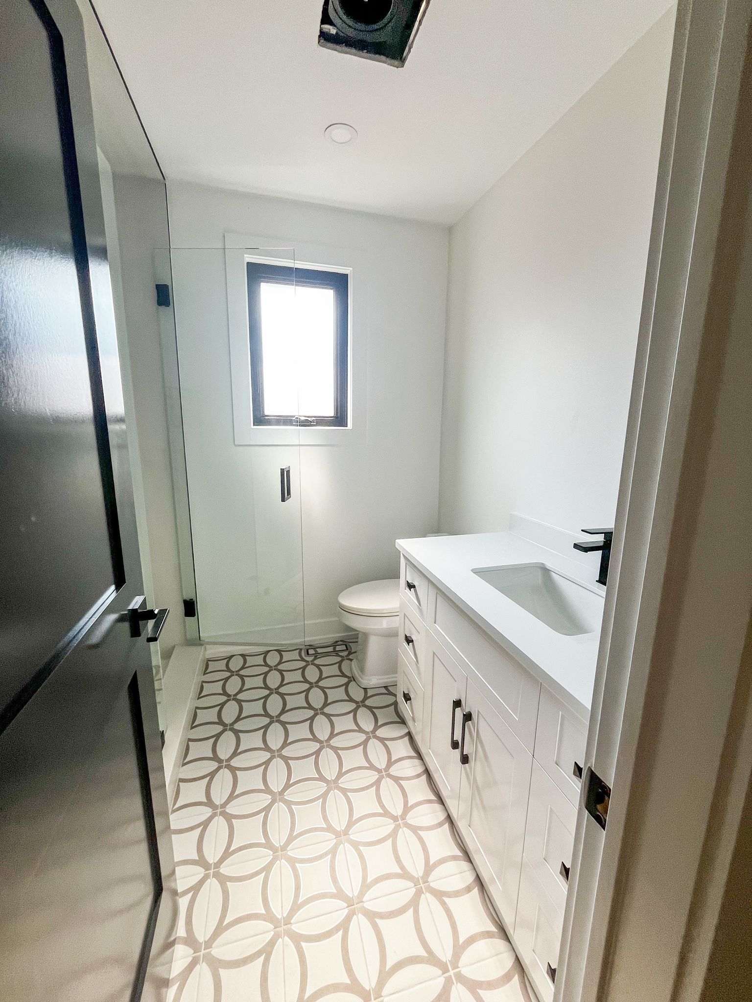 Small white bathroom with patterned floor, white vanity, and black door.
