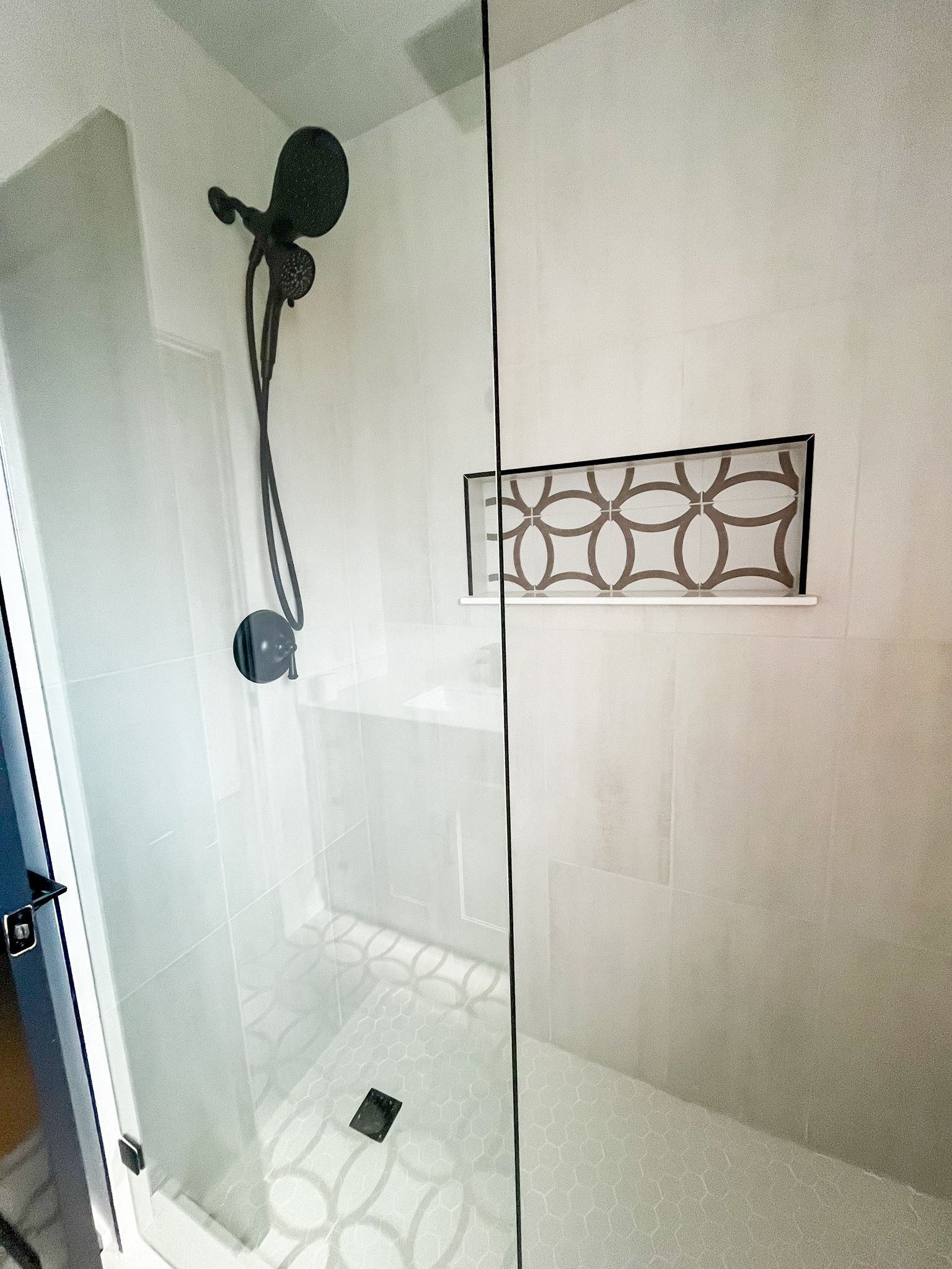 Modern shower with black fixtures, glass door, and patterned tile floor and wall niche.