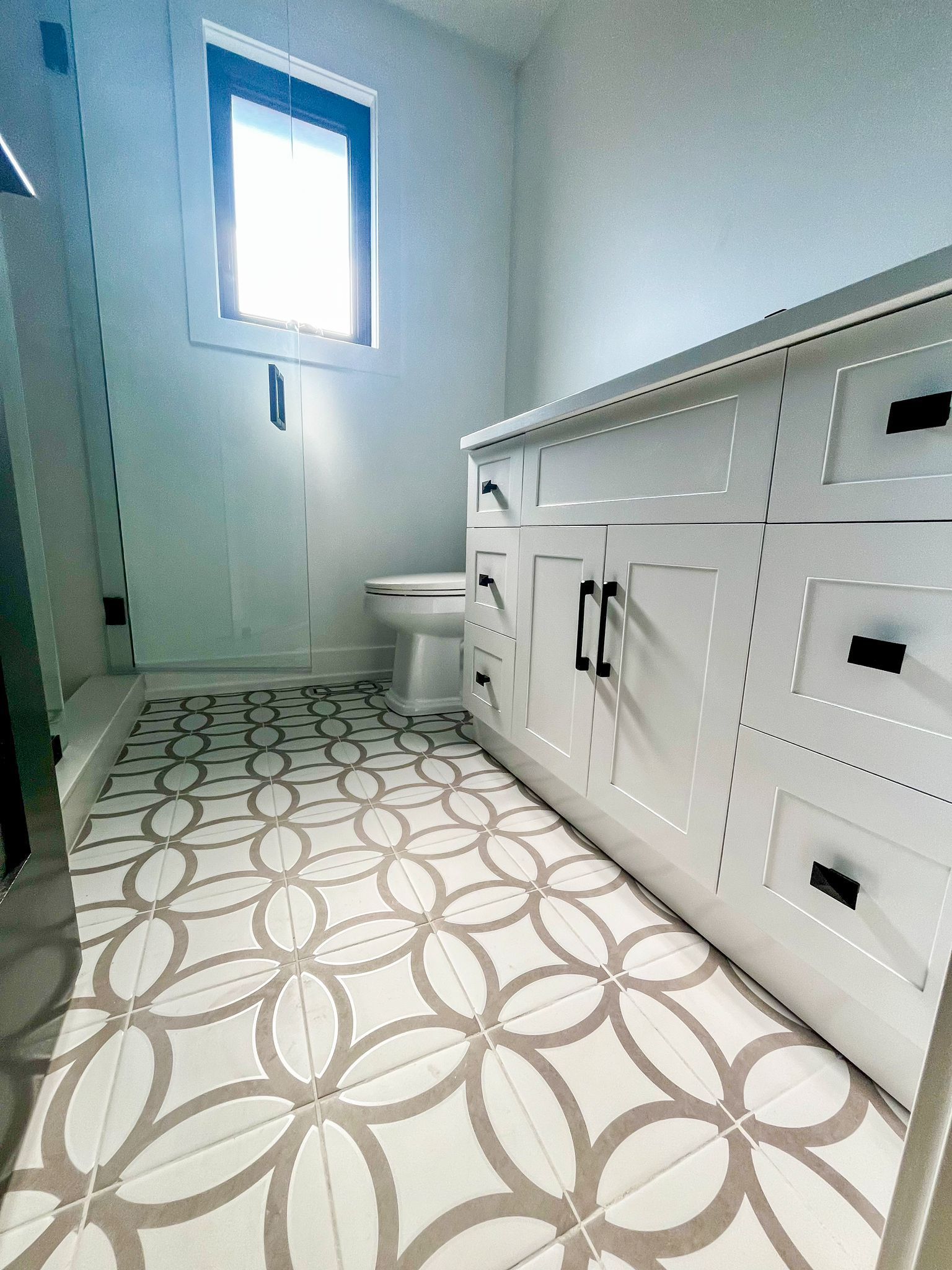 Bathroom with white vanity, patterned floor tiles, and a small window.