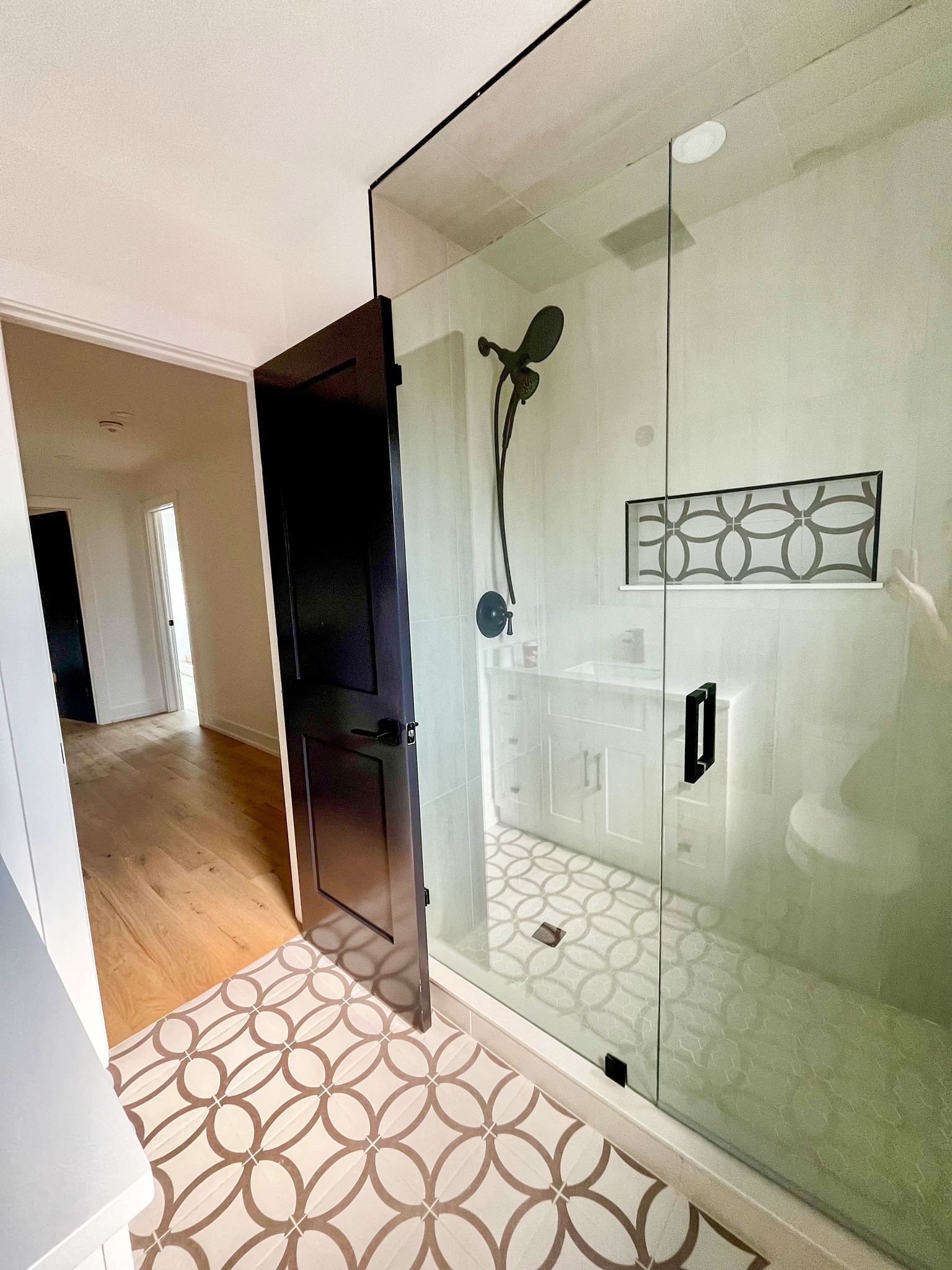 Bathroom with glass shower, patterned floor, and black door.