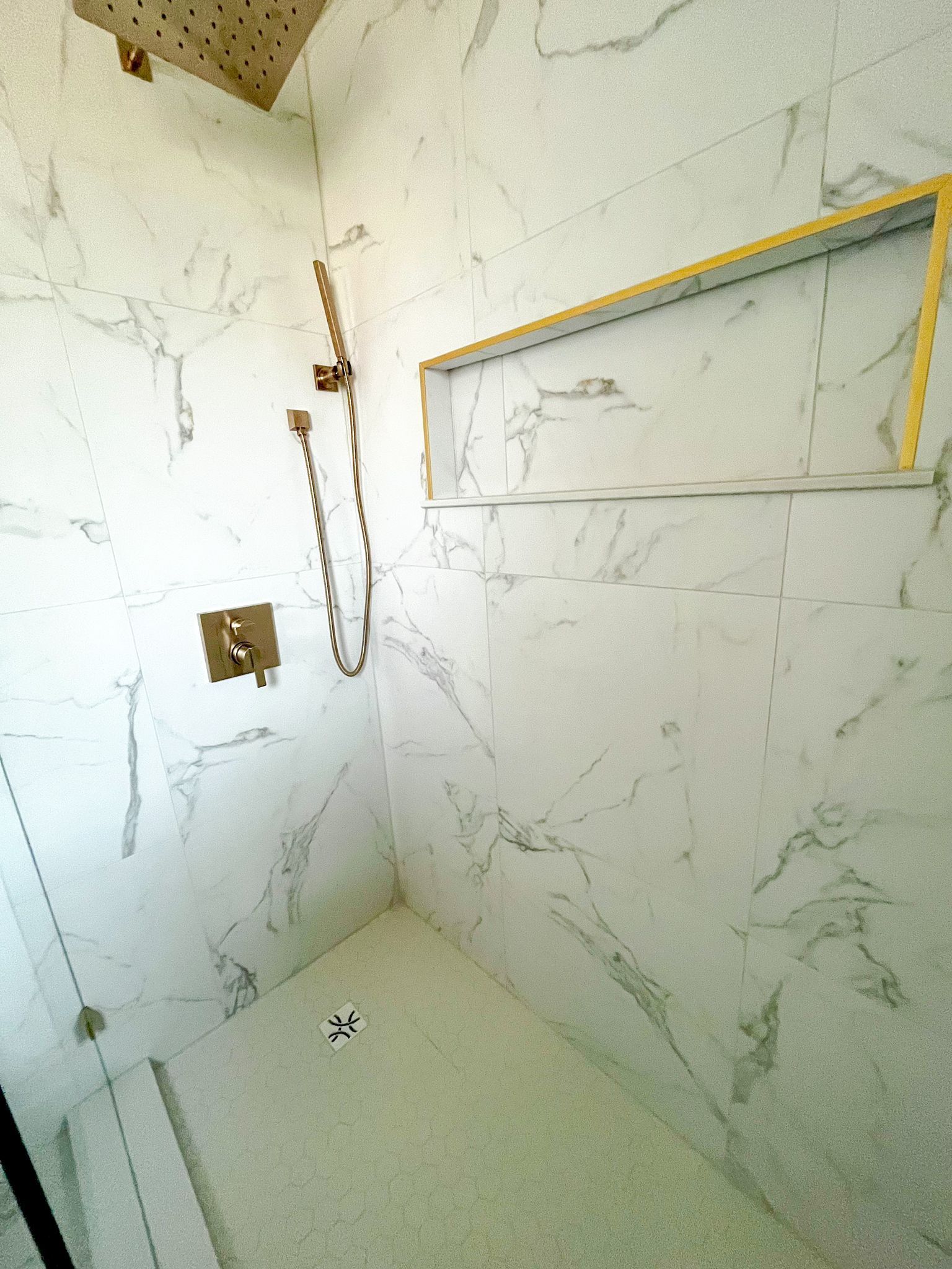 Shower with marble-look tiles, a gold shower head and fixture, and a built-in shelf.