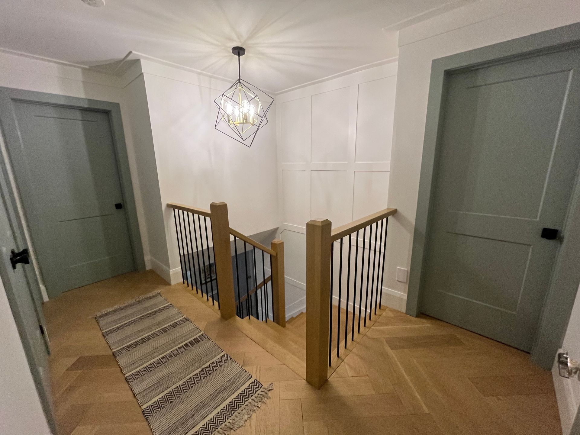 Hallway with two green doors, wooden staircase, and a geometric chandelier.