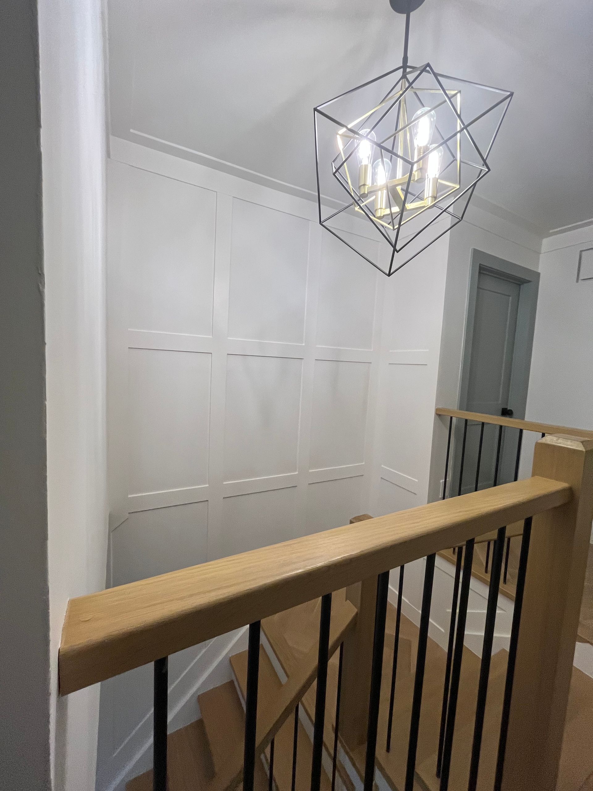 Staircase with wooden banister, black spindles, white walls, geometric light fixture.