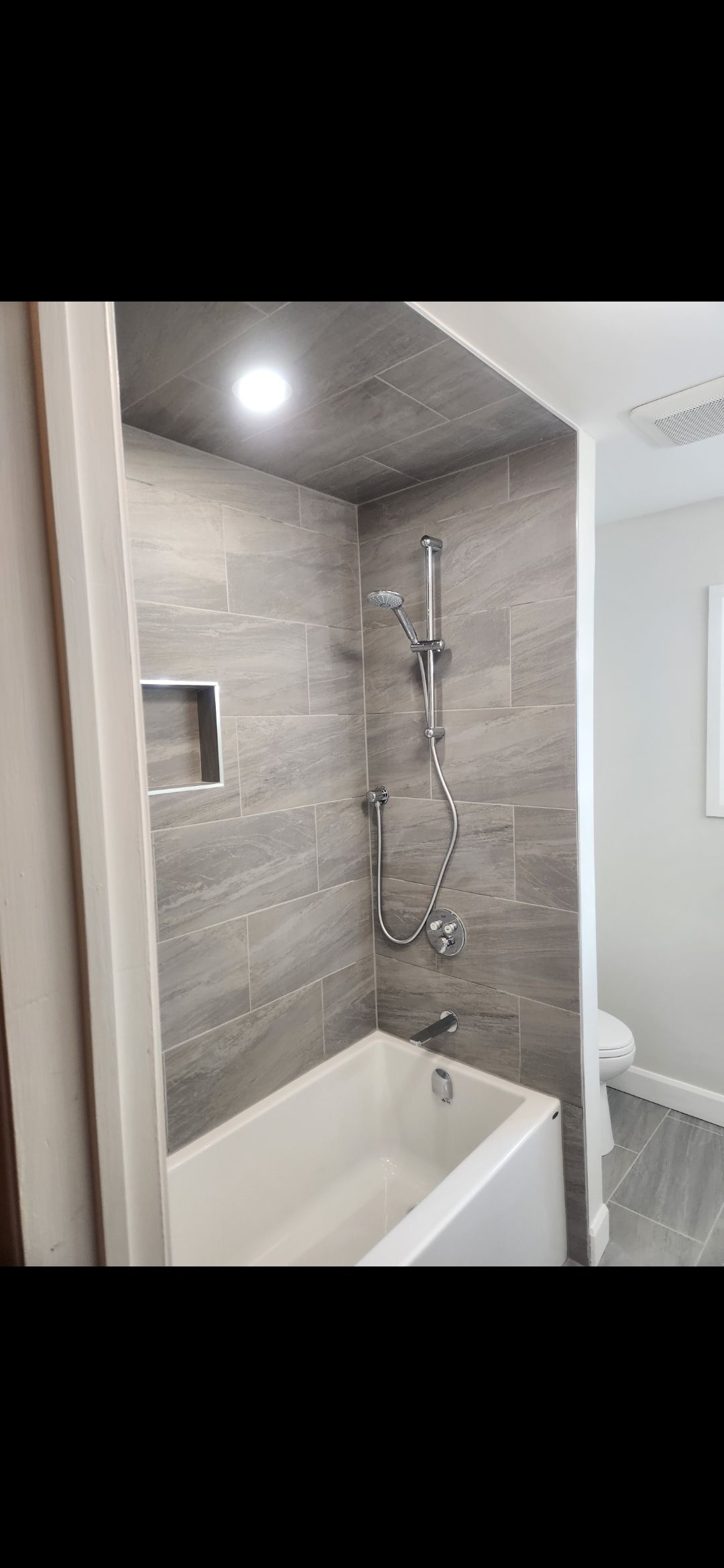 Bathroom with a gray-tiled shower and bathtub; a recessed shelf is built into the wall.
