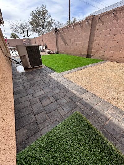 A brick walkway leading to a backyard with a lawn and a brick wall.