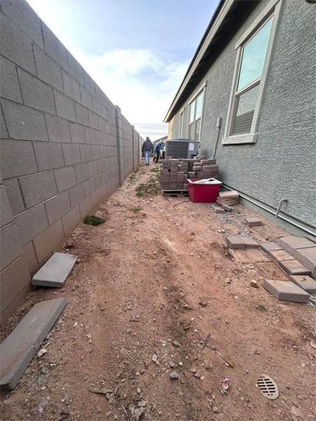 A dirt path leading to a house with a brick wall.
