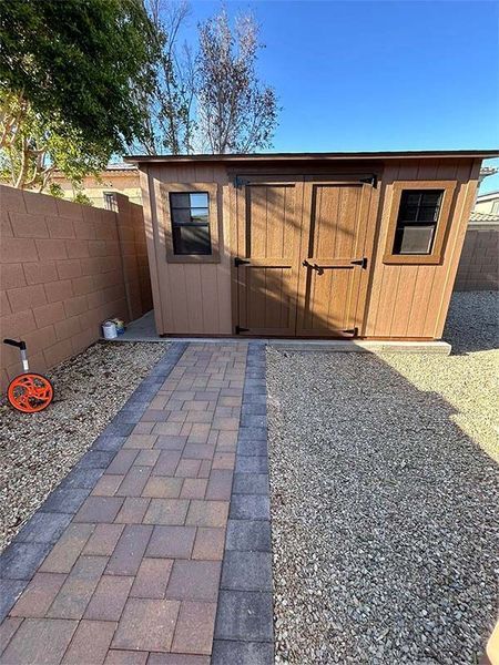 A wooden shed with a brick walkway leading to it