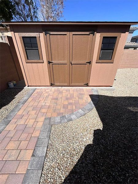 A brown shed with a brick walkway leading to it.
