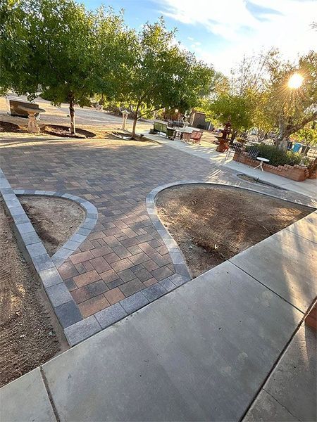 A brick walkway is being built next to a sidewalk in a park.