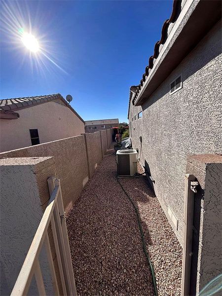 A walkway between two houses with gravel and a fence.
