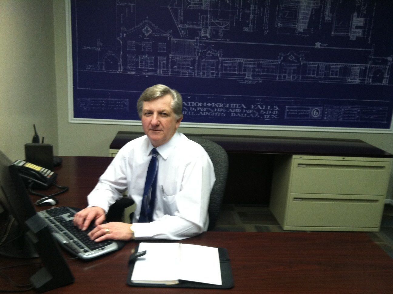A man sits at a desk in front of a blueprint