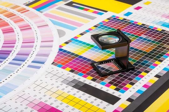 A magnifying glass is sitting on top of a bunch of colorful papers.