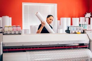 A woman is holding a roll of paper in front of a printer.