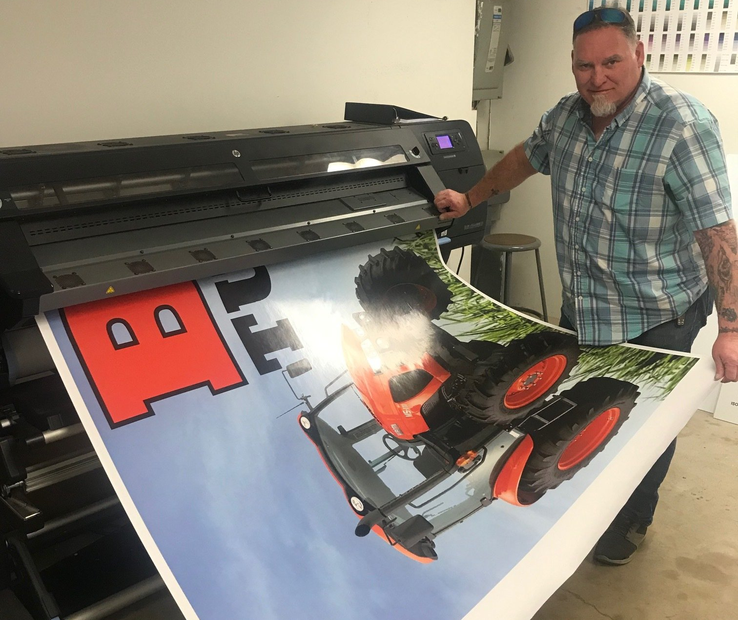 A man is holding a large poster of a tractor in front of a printer.