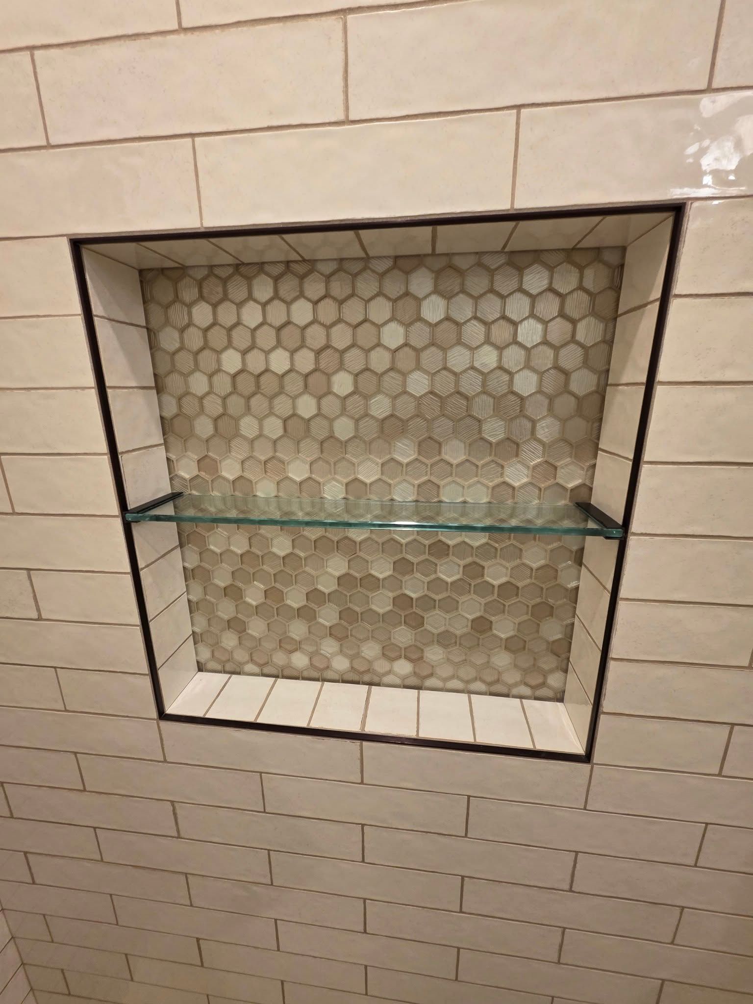 A shower niche with a glass shelf in a bathroom.