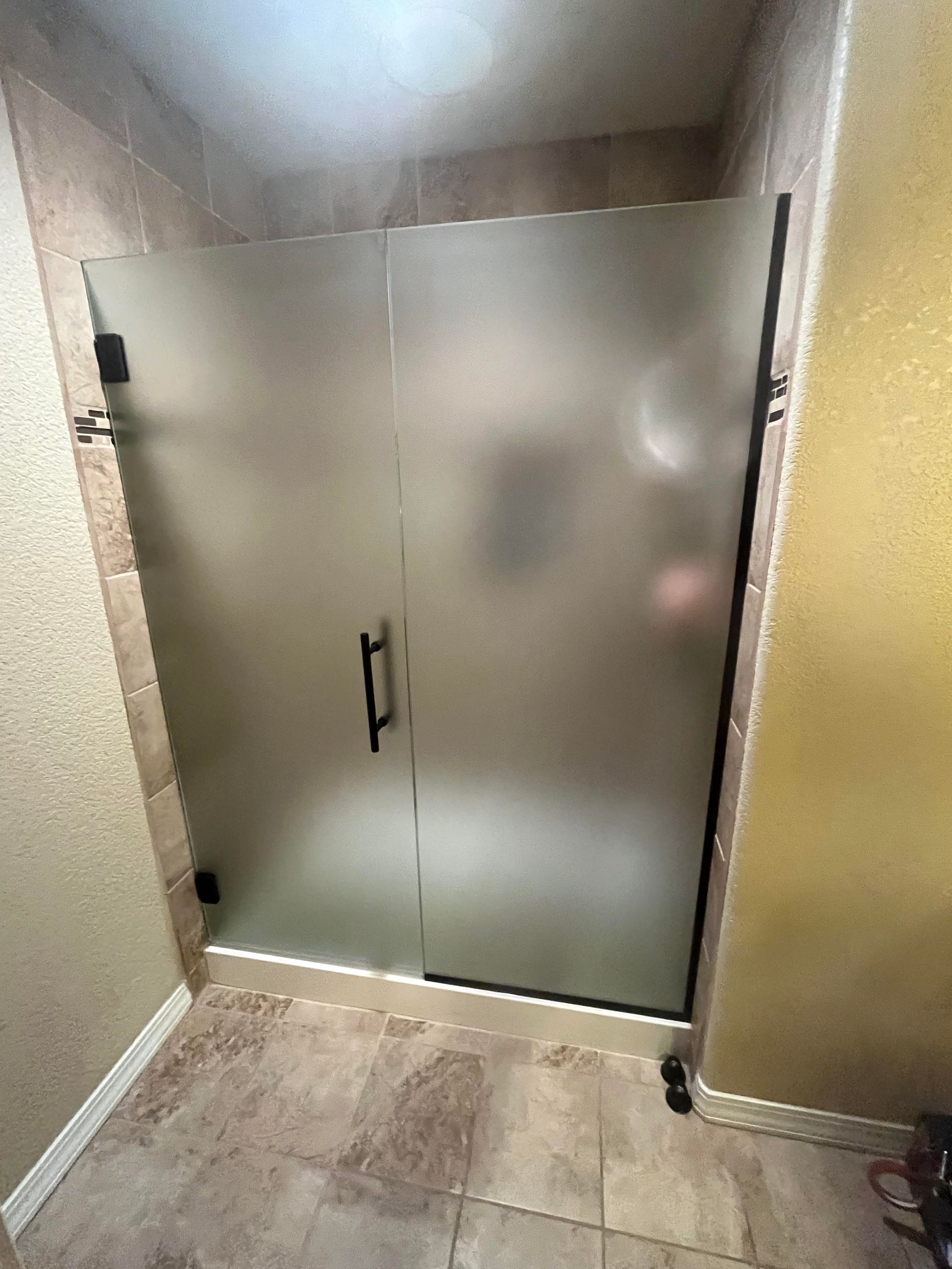 A bathroom with a shower stall with a frosted glass door.