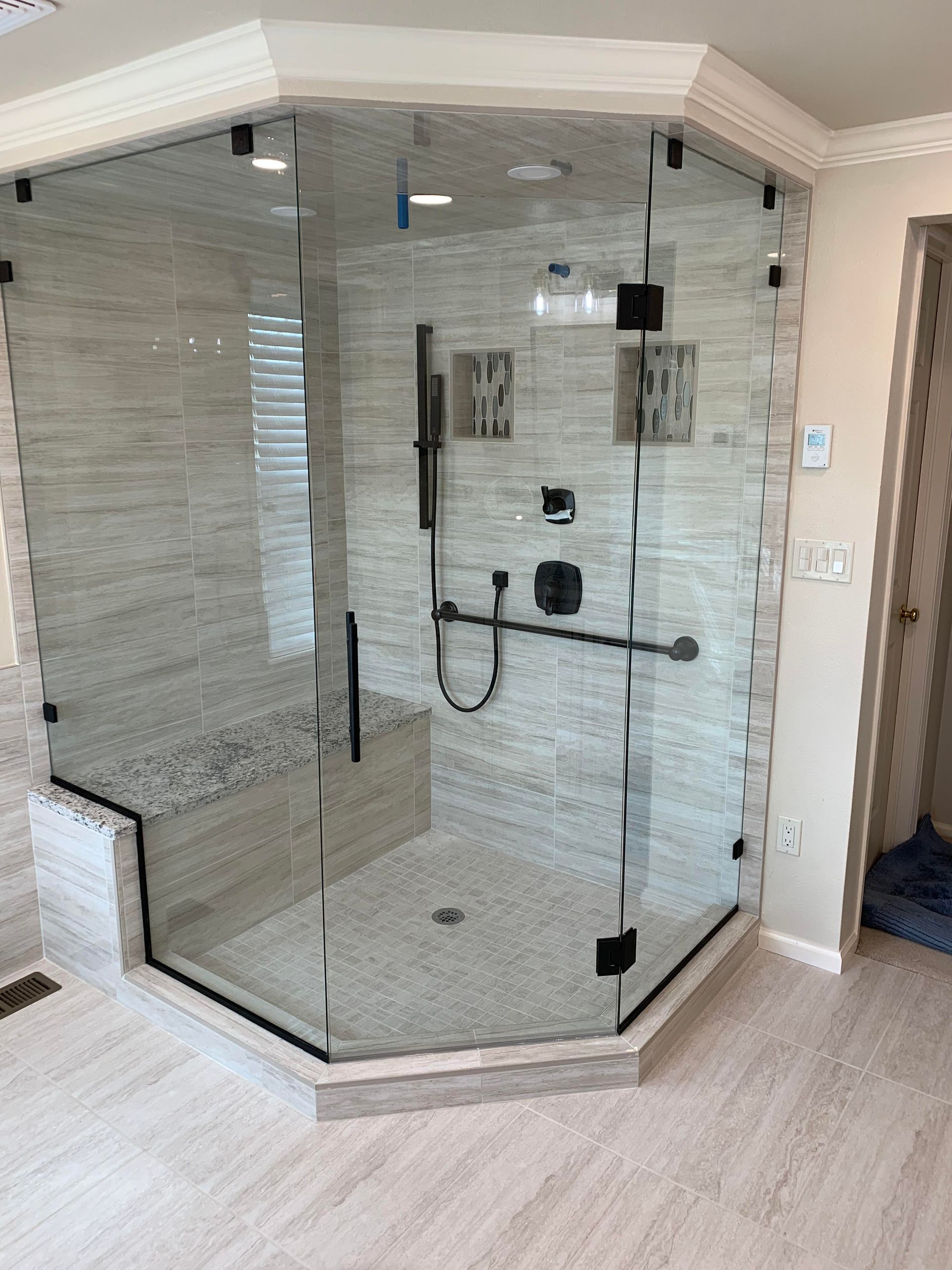 A bathroom with a glass shower door and a bench.