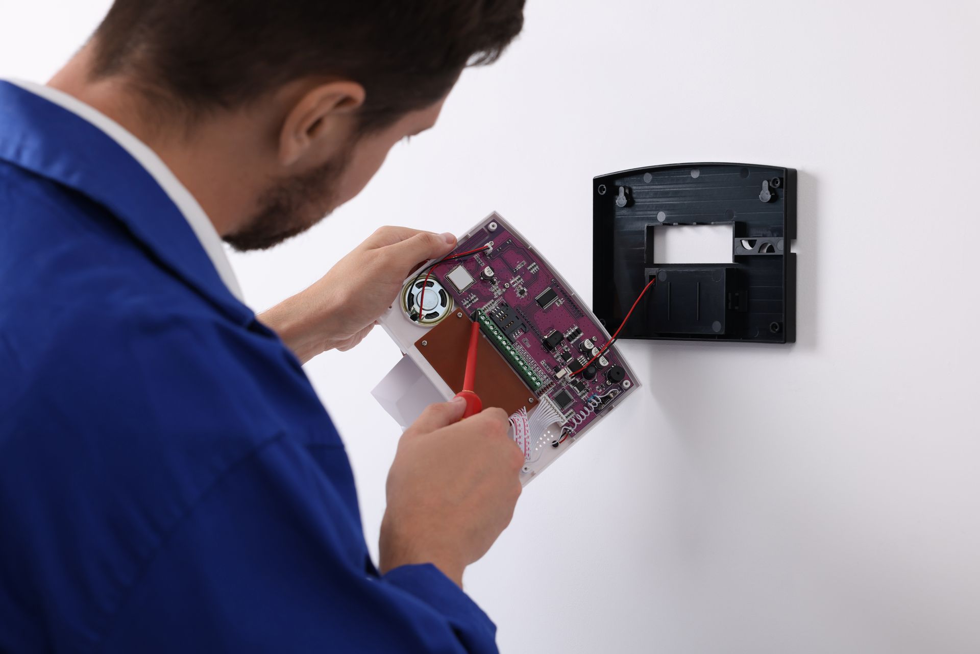 Un technicien en uniforme bleu installe un panneau de commande électronique mural dont le circuit imprimé est apparent.