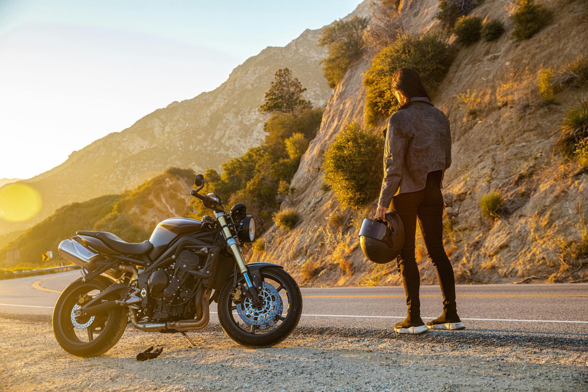 A man is standing next to a motorcycle on the side of the road.